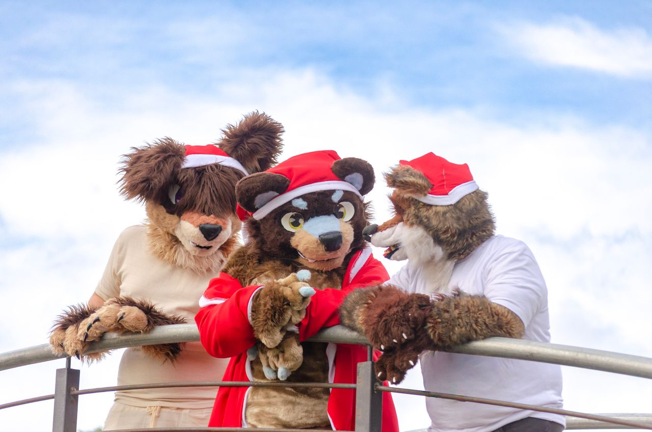 Three people in furry costumes with Santa hats enjoy a fun outdoor moment in Montevideo.